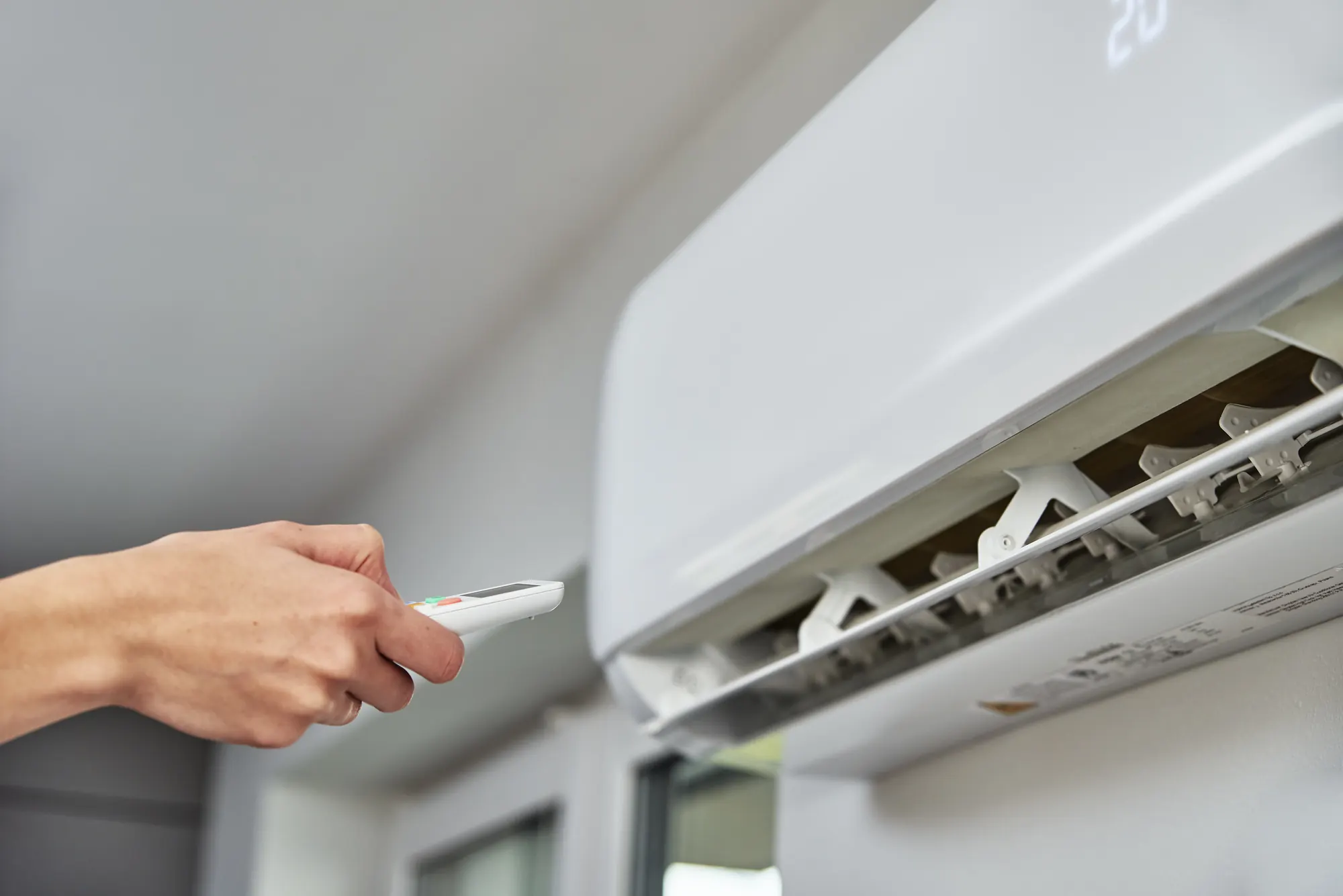 Mano con el mando a distancia ajustando la temperatura de un aire acondicionado de pared